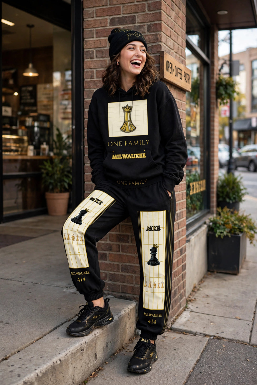 Milwaukee outfit worn — black Milwaukee hoodie with king panel stack, black v9 joggers, black and gold beanie, leaning at a storefront